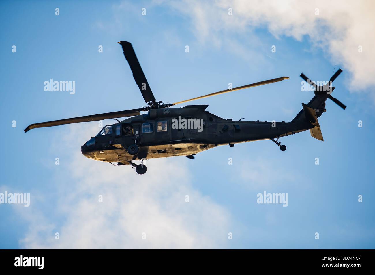 Bewaffneter Hubschrauber mit taktischem Rumpf, Doppelrotor-System und Unterbauchausrüstung in klarer Luftbewegung gegen den beleuchteten Himmel Stockfoto