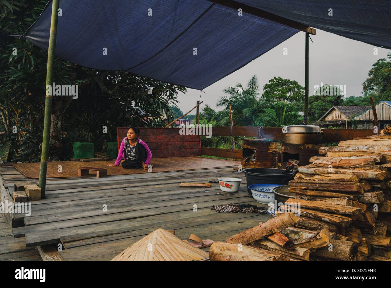 West Kutai, Indonesien - 11. Oktober 2025. Eine Dayak-Frau sitzt unter einem Bambusschutz in der Nähe eines traditionellen Holzofens im Dorf Mancong, East Kali Stockfoto