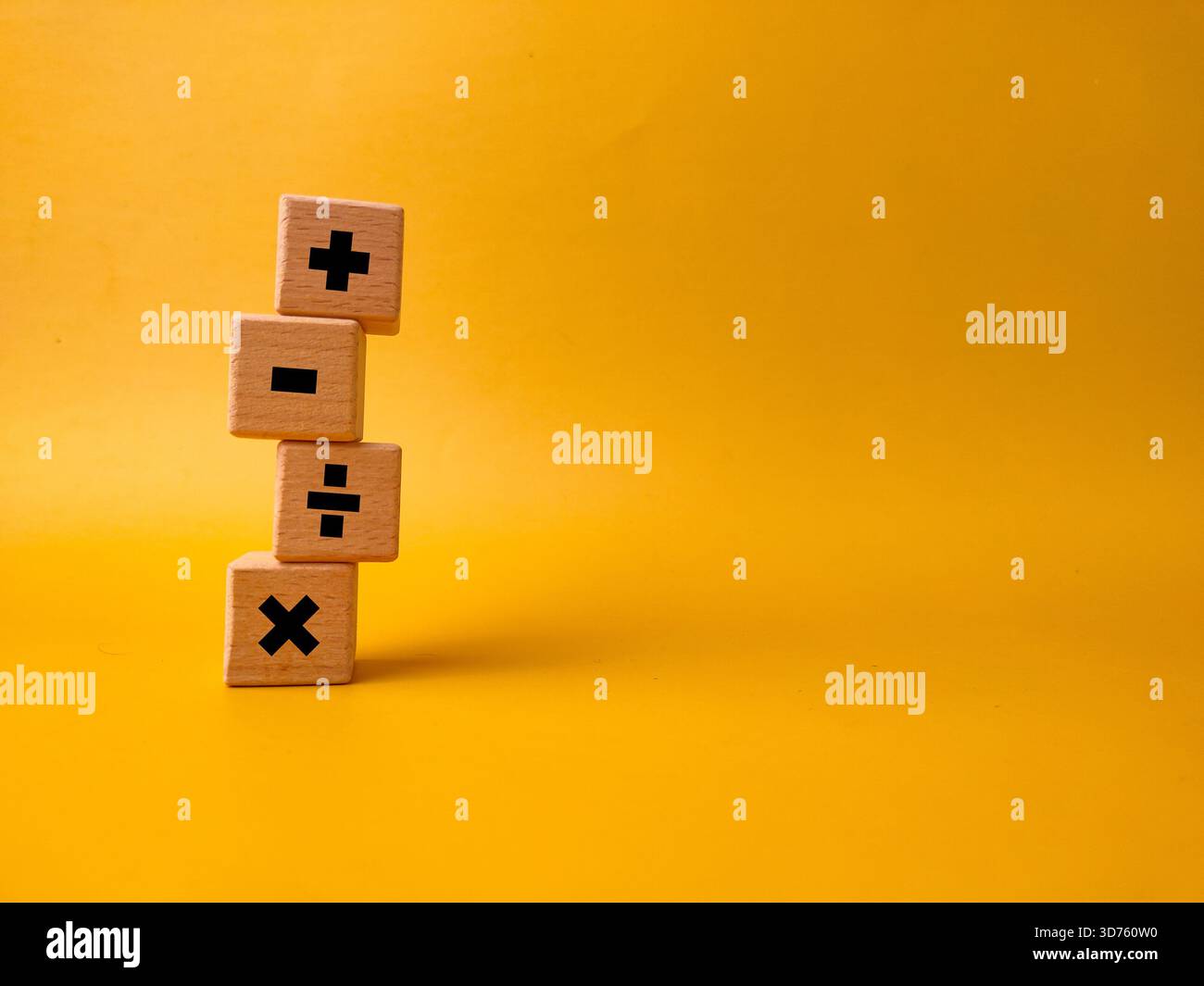 Das Bild zeigt vier Holzblöcke mit grundlegenden mathematischen Betriebssymbolen auf gelbem Hintergrund. Stockfoto