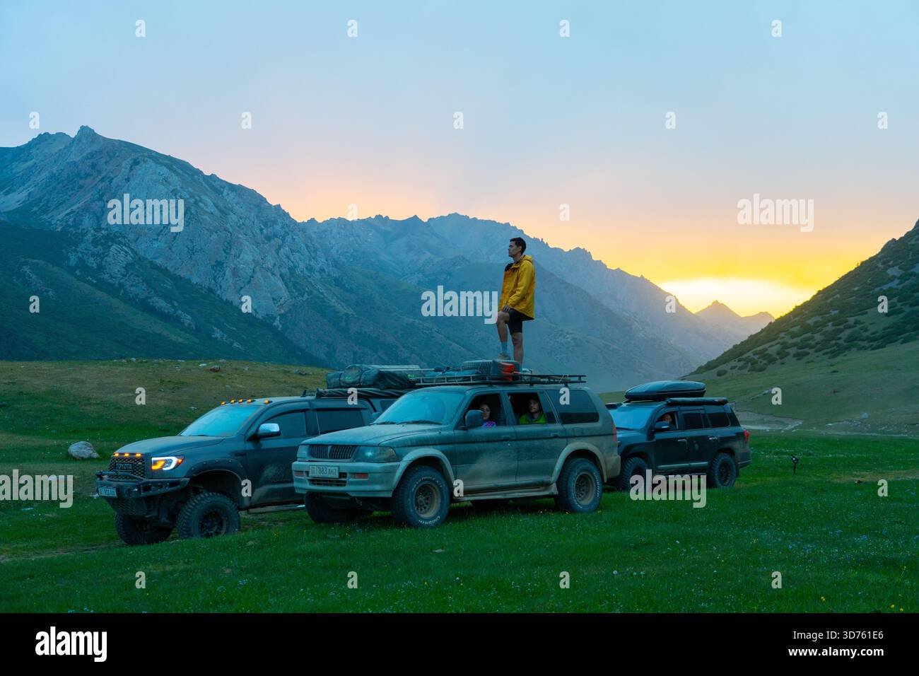 Talas, Kasachstan – 13. Mai 2024: Ein Kaukasier in gelber Jacke auf dem Dachträger eines geparkten Geländewagens steht und den Bergwettkampf vermisst Stockfoto
