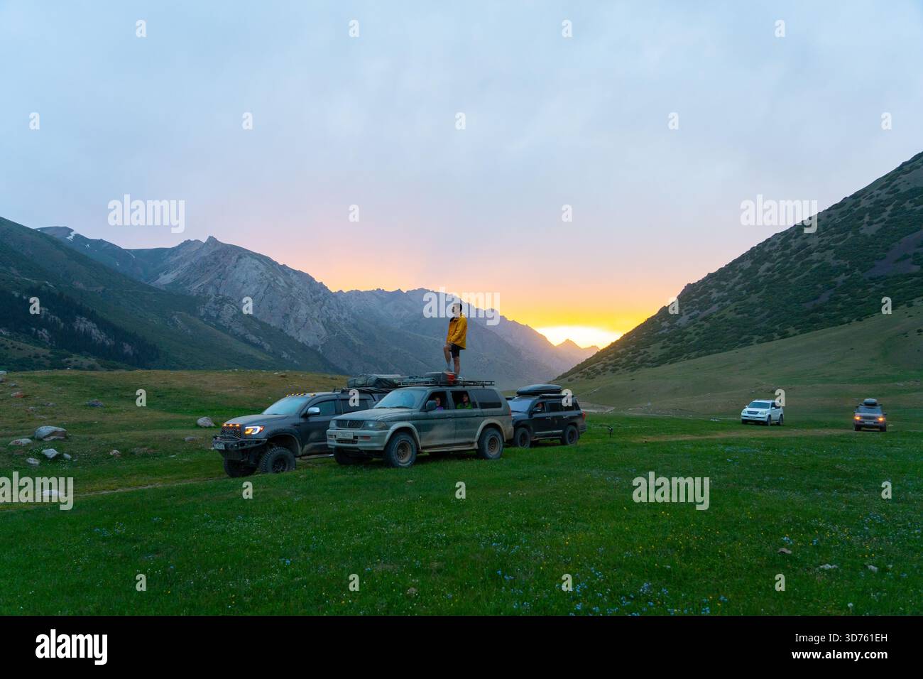 Talas, Kasachstan – 13. Mai 2024: Ein Konvoi von Geländefahrzeugen parkte bei Sonnenuntergang auf einer Bergwiese mit einem Kaukasier auf einem Dachträger. Zwei Stockfoto
