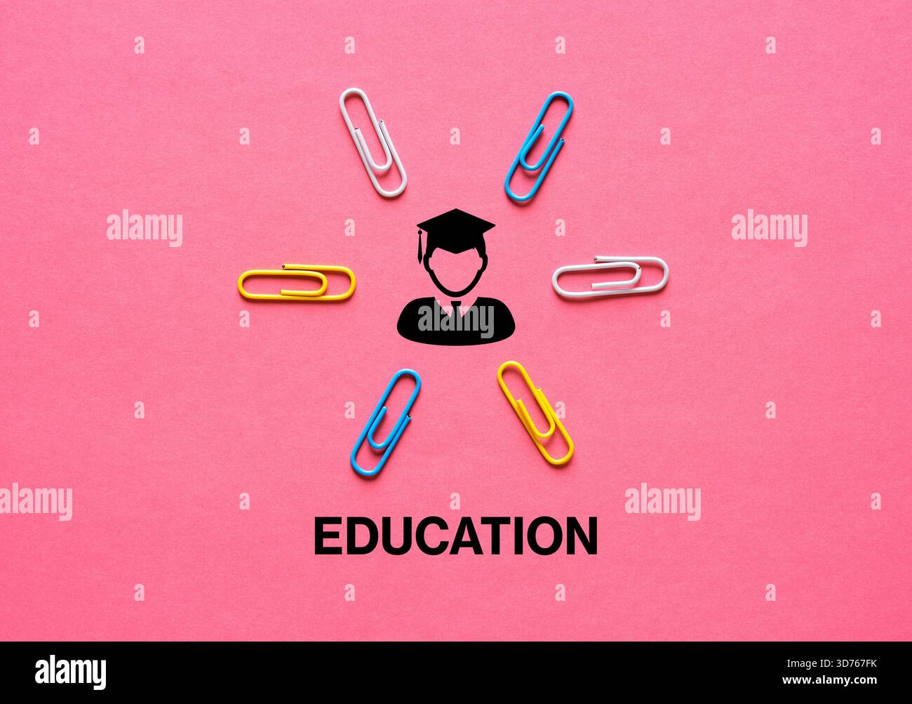 Bildungskonzept, dargestellt durch ein schwarzes Graduierungssymbol, umgeben von bunten Büroklammern auf rosa Hintergrund Stockfoto