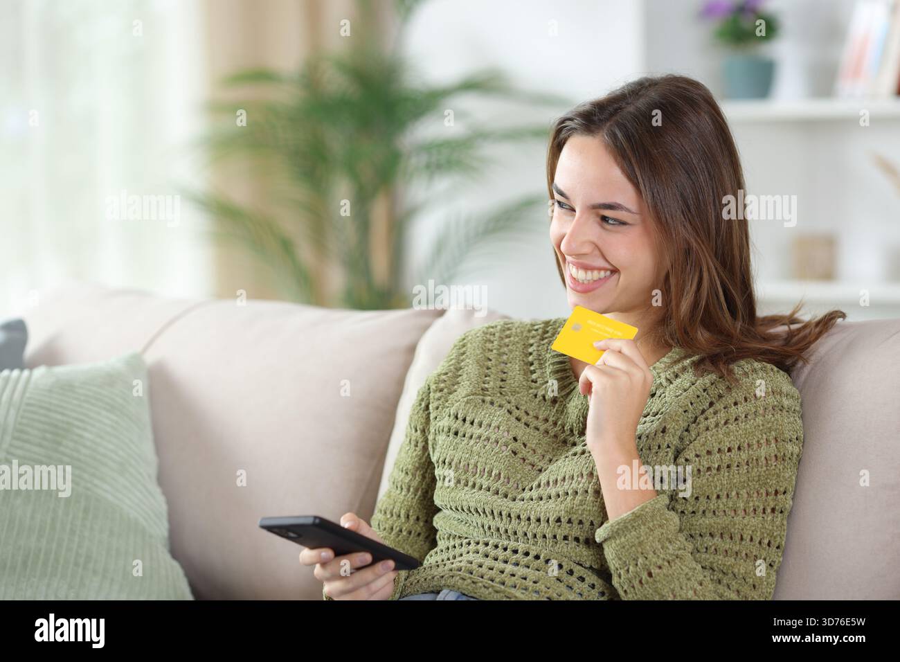 Glückliche Frau in grünem Denken und online kaufen mit Kreditkarte und Telefon auf einem Sofa zu Hause Stockfoto