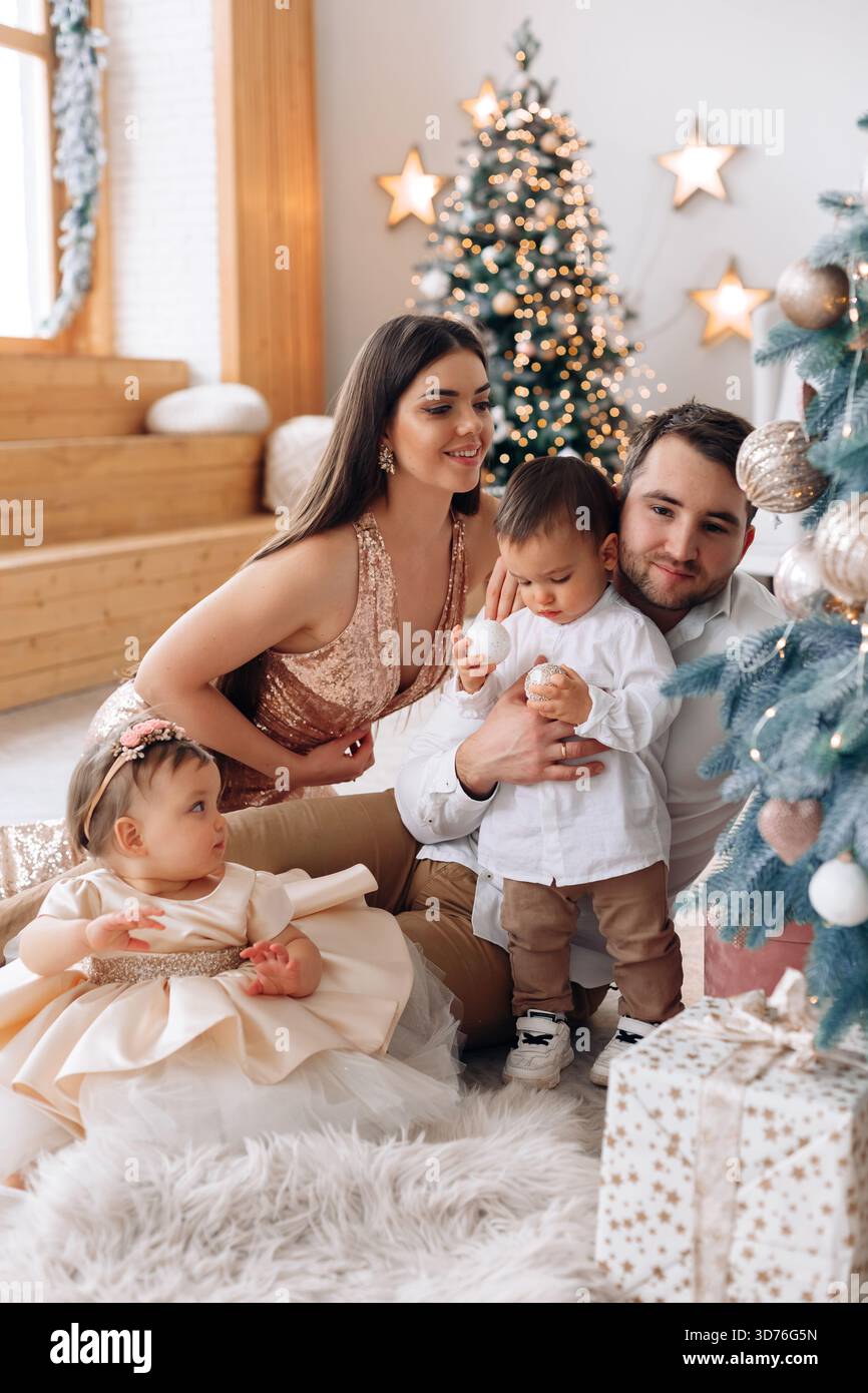 Eine fröhliche Familie versammelt sich um einen Weihnachtsbaum und genießt die gemeinsame Zeit. Kleine Kinder spielen, während Erwachsene in einem warmen, festlichen Ambiente zusehen und lächeln Stockfoto