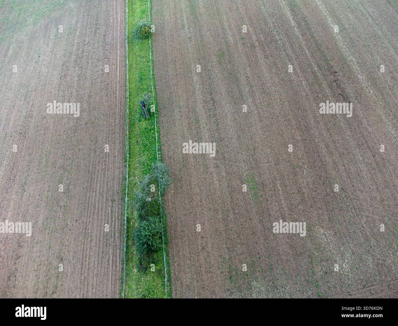 Ein breiter Luftschuss von oben nach unten von zwei großen gepflügten braunen Feldern, geteilt durch einen schmalen grünen Streifen von Gras und kleinen Bäumen. Das geometrische Muster und die Längen Stockfoto