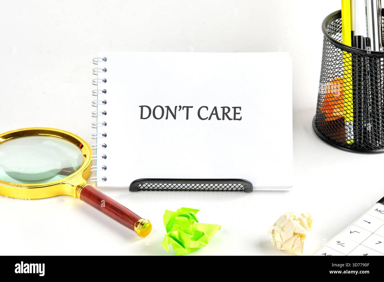Ein Notizbuch steht offen und zeigt „Do t Care“ an. Daneben befinden sich zerknittertes Papier, eine Lupe, Bleistifte in einem Halter und ein Taschenrechner auf einer weißen Brandung Stockfoto