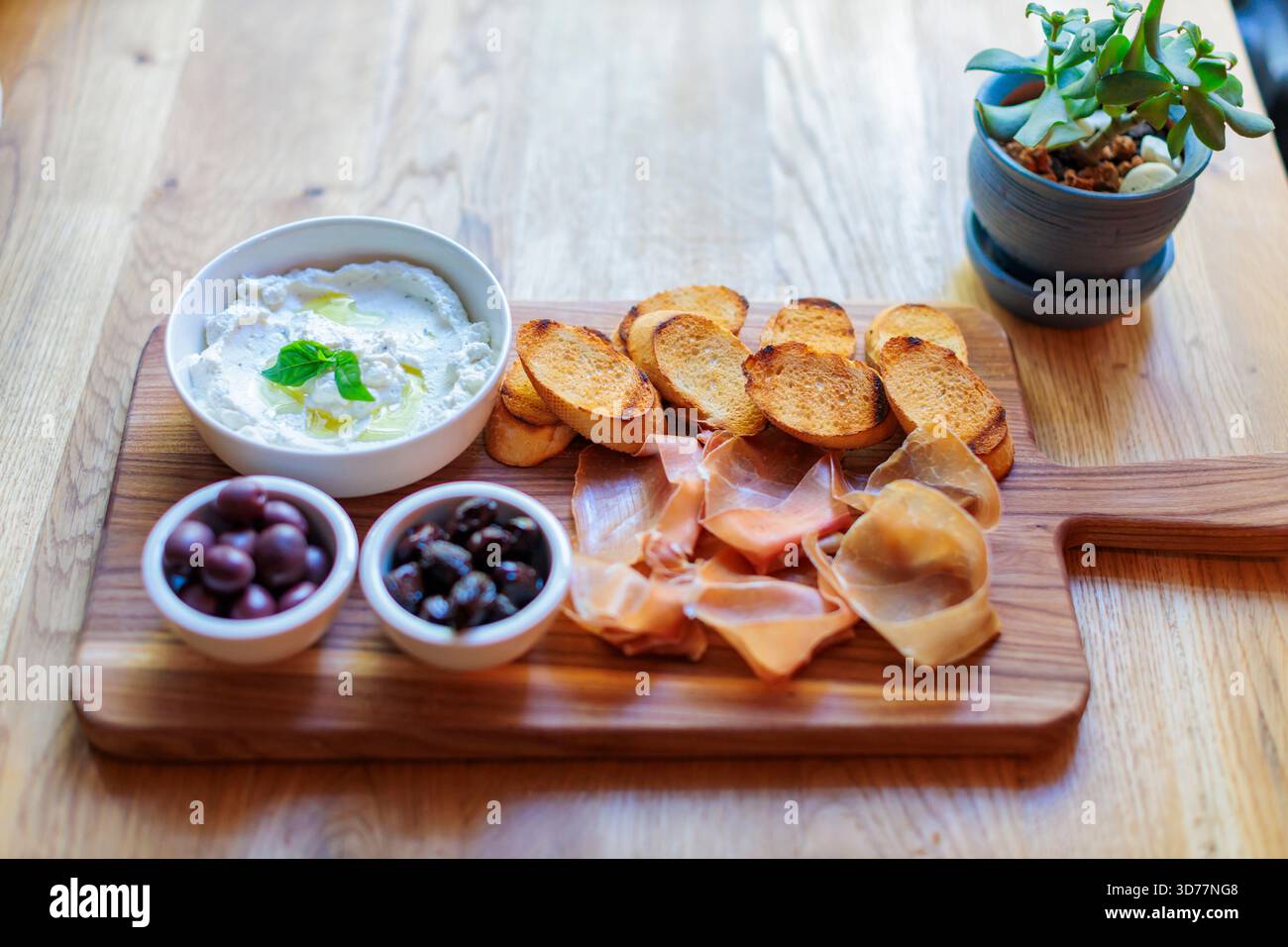 Gegrilltes Brot, Schinken, Ricotta-Aufstrich und Oliven auf einem Schneidebrett Stockfoto