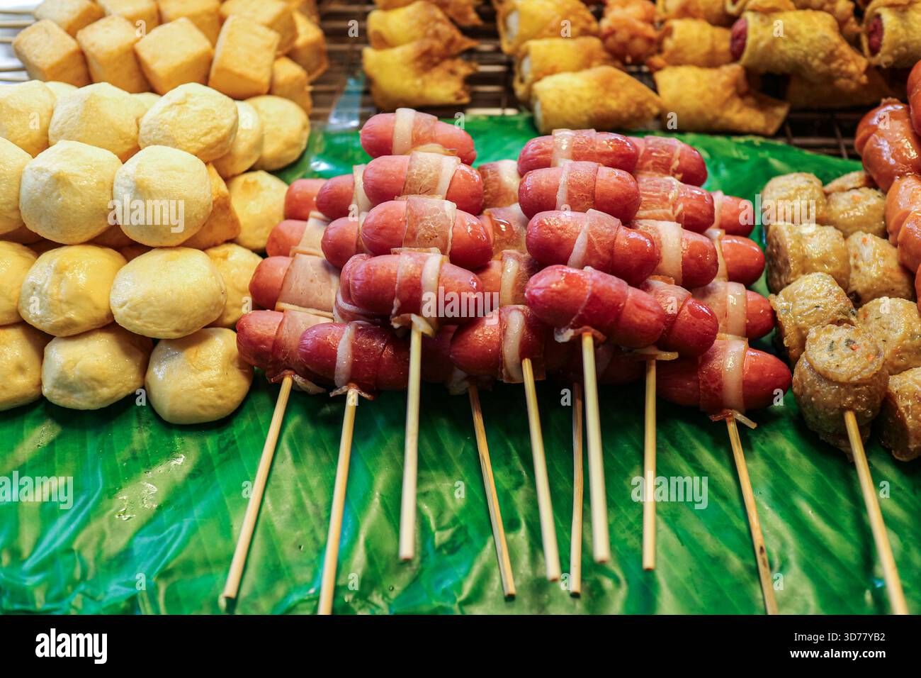 Verschiedene thailändische Straßensnacks auf Spießen, einschließlich Speckwurst, Schweinetofu-Fleischbällchen, Krabbenbrötchen, gebratene Knödel auf Bananenblättern. Stockfoto