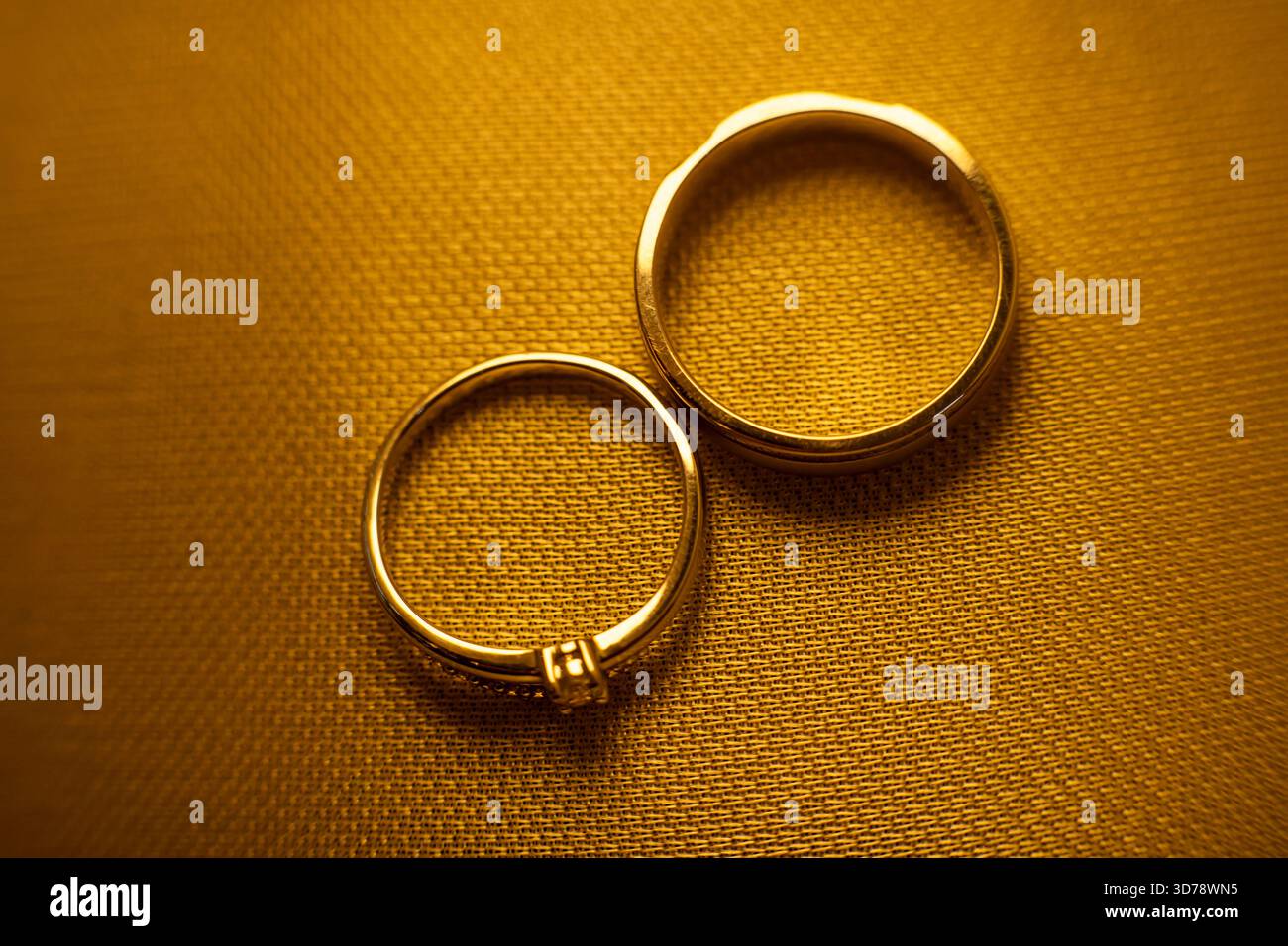 Schließen Sie zwei goldene Hochzeitsringe auf strukturiertem Stoffhintergrund Stockfoto