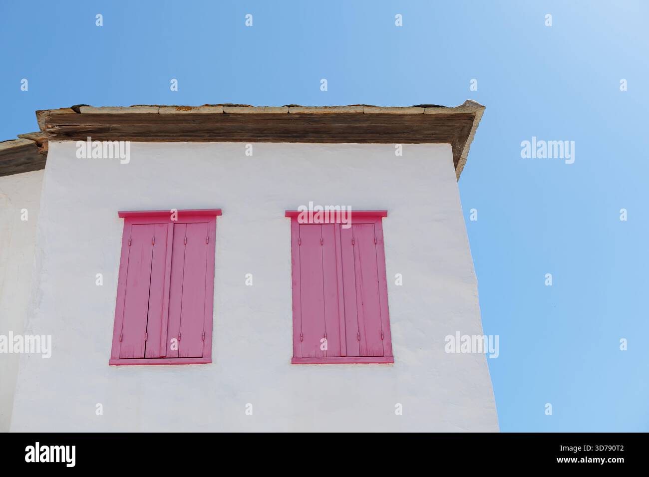 Weißes Gebäude mit pinkfarbenen Holzläden vor blauem Himmel Stockfoto