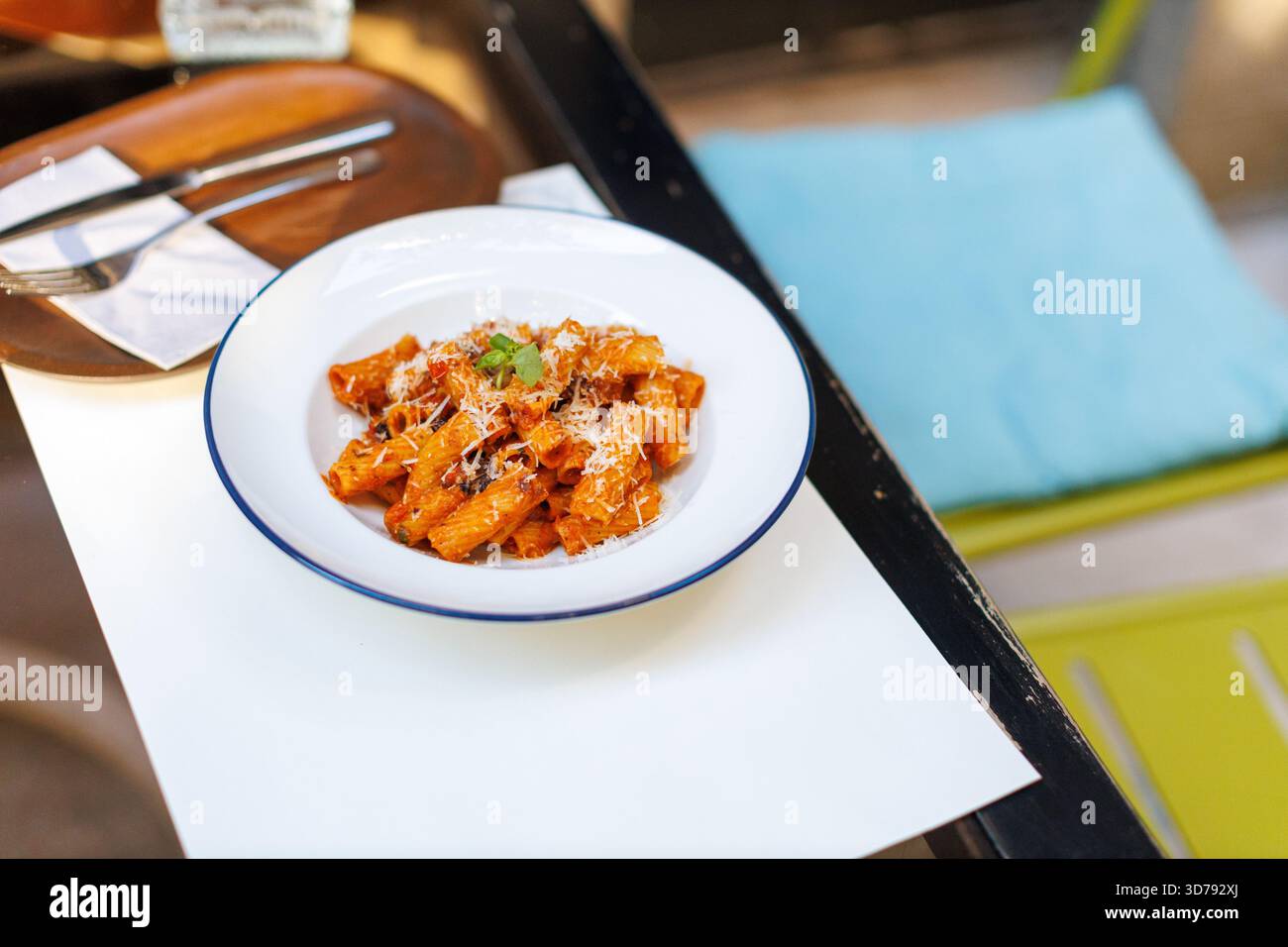 Köstliche Rigatoni-Pasta mit frischem Basilikum und Käse serviert auf einem rustikalen Tisch in gemütlicher Atmosphäre im Freien Stockfoto