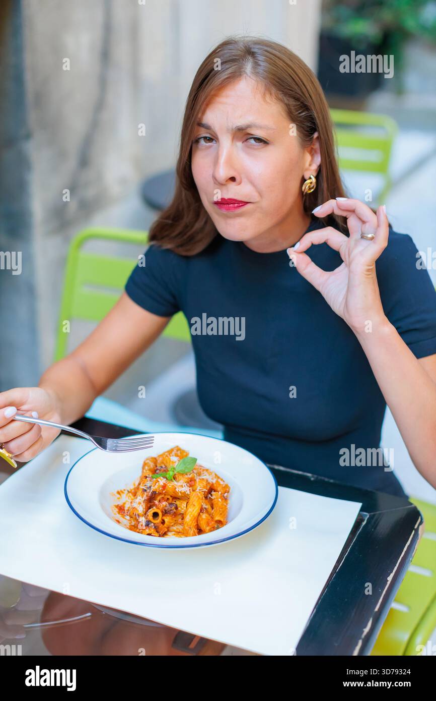 Junge Frau, die an einem sonnigen Tag köstliche Pasta in einem Café im Freien genießt und jeden Happen mit einem zufriedenen Ausdruck genießt Stockfoto