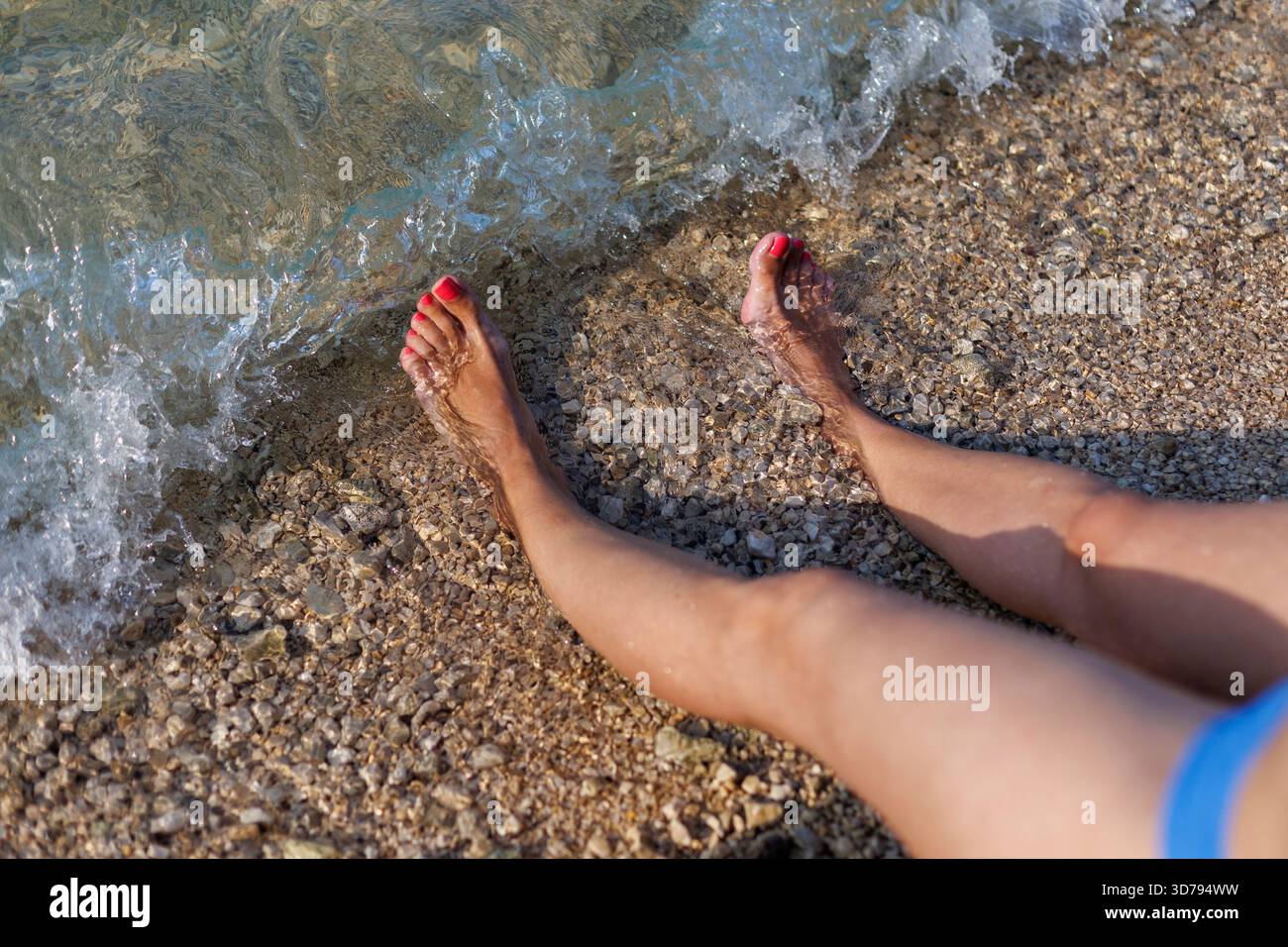 Entspannen Sie am Ufer mit Zehen im Wasser an einem Sandstrand an einem sonnigen Tag Stockfoto