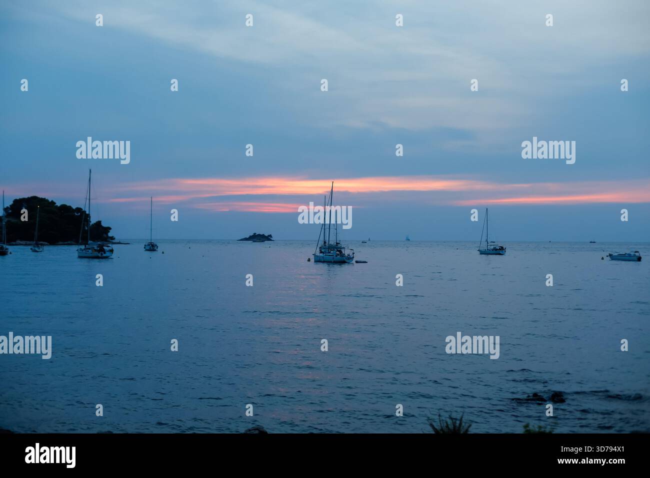 Wunderschöne Dämmerung über einer ruhigen Bucht mit Segelbooten, die bei Sonnenuntergang im ruhigen Wasser ankern Stockfoto