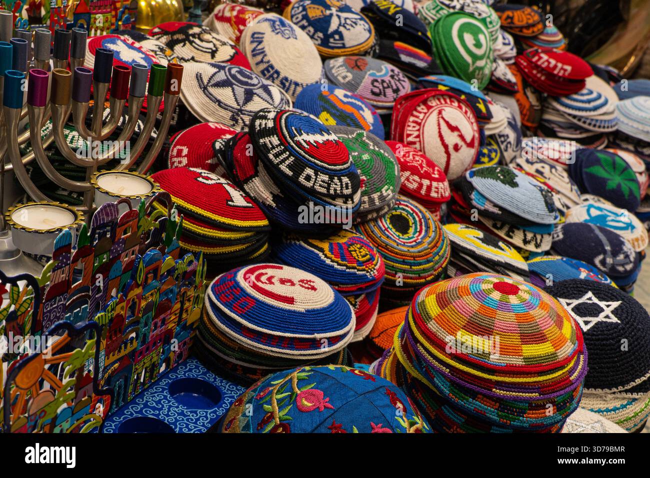Nahaufnahme eines Marktstandes in Jerusalem, der gestrickte Kippahs (כיפה סרוגה) verkauft, mit farbenfrohen Kopfbedeckungen und lebhafter Marktatmosphäre. Stockfoto