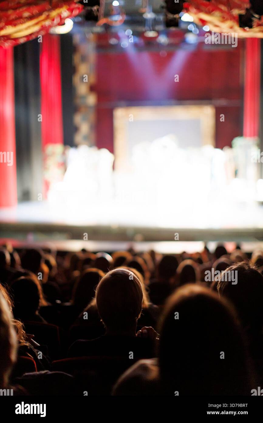 Publikum bei Theatervorstellung mit roten Vorhängen und hellen Bühnenlichtern Stockfoto