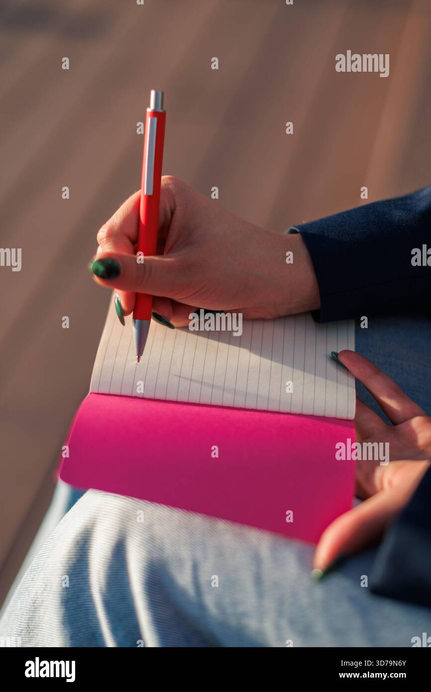 Nahaufnahme einer Person, die während des Sonnenuntergangs in rotem Notizbuch mit buntem Stift schreibt Stockfoto