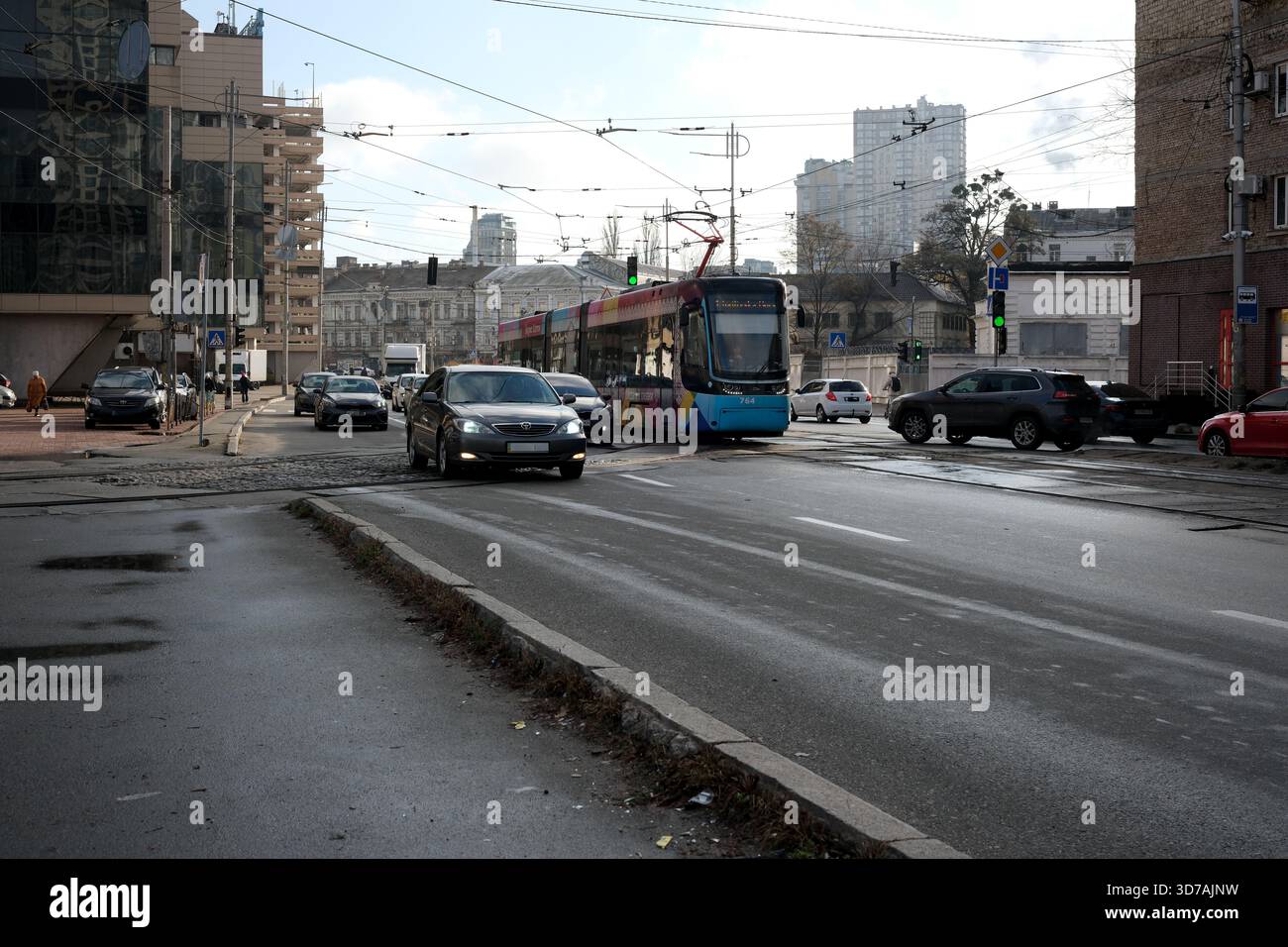Eine farbenfrohe Straßenbahn fährt durch eine städtische Kreuzung mit Autos in der Nähe. November 2025 Kiew, Ukraine Stockfoto