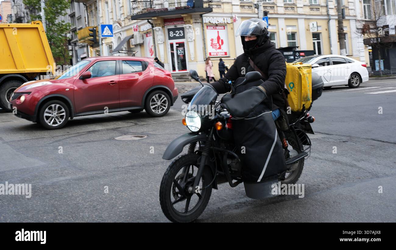 Ein Lieferfahrer fährt durch eine geschäftige Kreuzung, während er Pakete transportiert. November 2025 Kiew, Ukraine Stockfoto