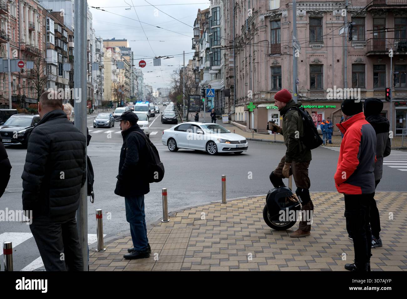 An einer Straßenecke versammeln sich Leute, die darauf warten, dass der Verkehr an einem bewölkten Morgen vorbeikommt. November 2025 Kiew, Ukraine Stockfoto