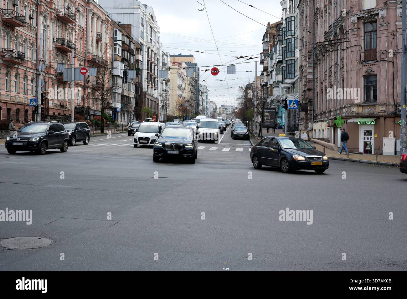 Autos fahren durch eine geschäftige Stadtstraße, gesäumt von historischen Gebäuden, während Fußgänger zu Fuß laufen. November 2025 Kiew, Ukraine Stockfoto