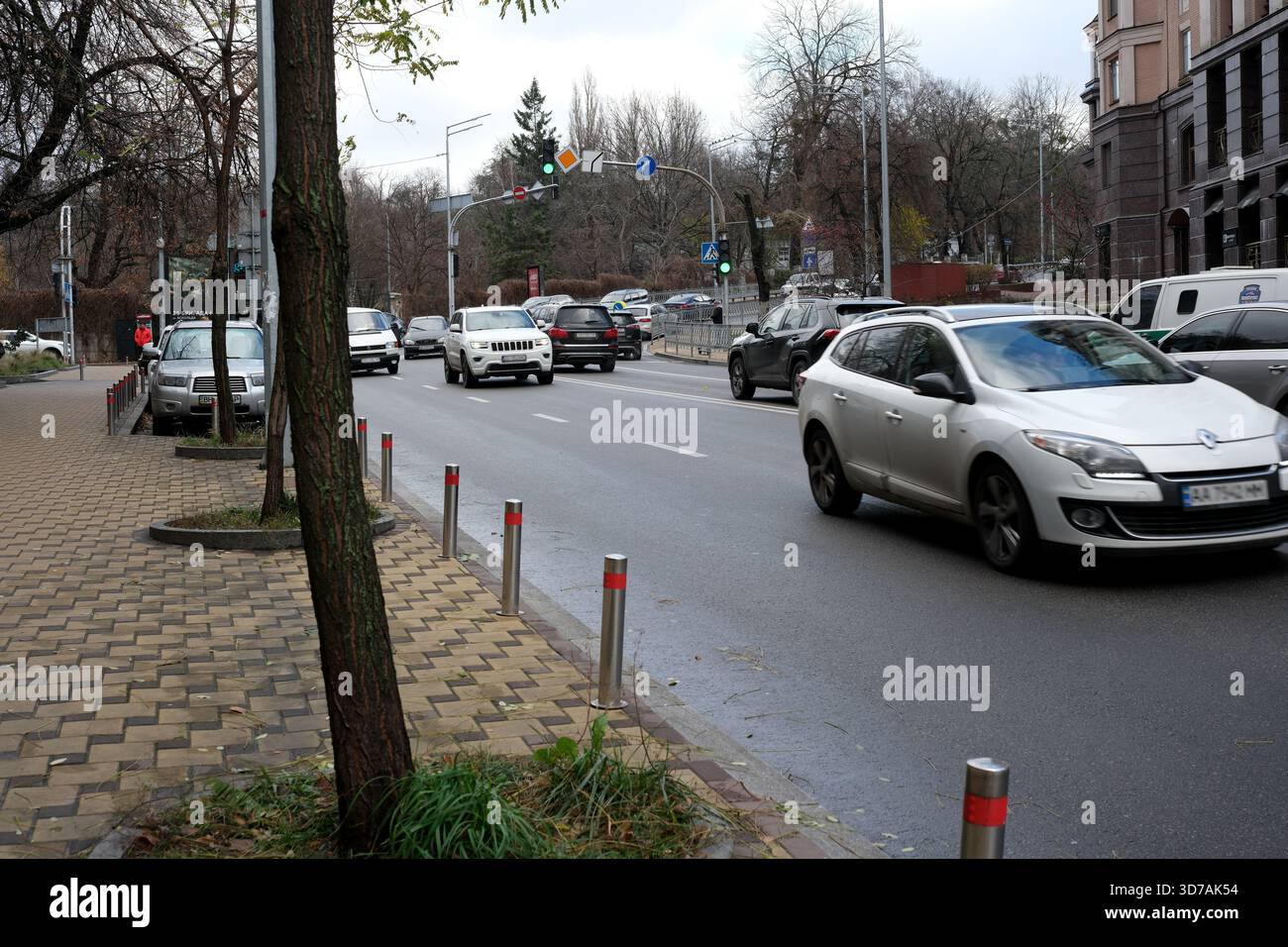 Autos fahren durch eine belebte Straße, die von Bäumen und Gebäuden gesäumt ist, unter grauem Himmel. November 2025 Kiew, Ukraine Stockfoto