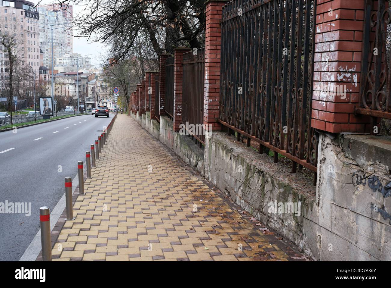 Ein gepflasterter Weg säumt die Straße neben einer historischen Backsteinmauer, die das Leben der Stadt symbolisiert. November 2025 Kiew, Ukraine Stockfoto