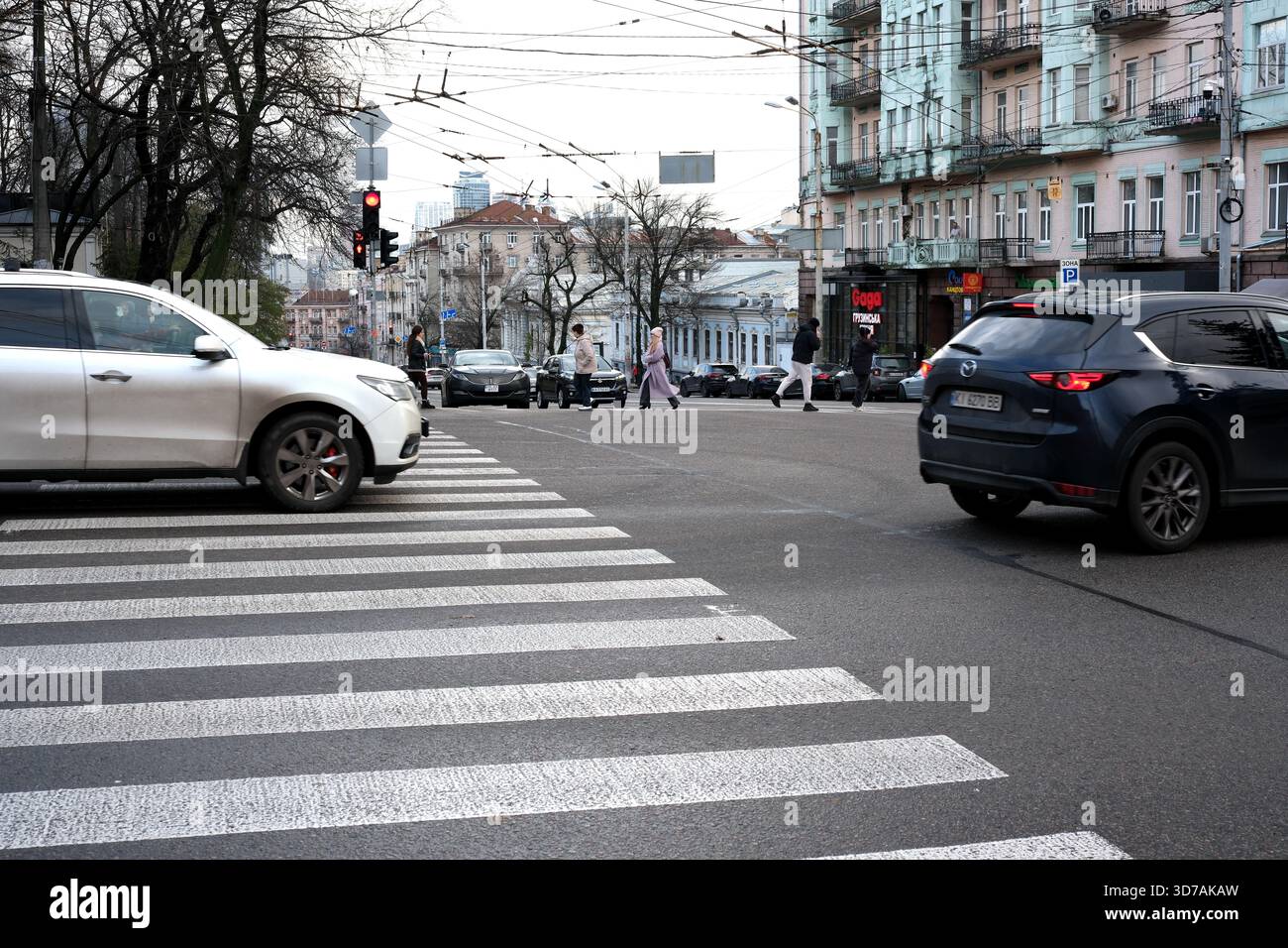 Fahrzeuge fahren durch eine geschäftige Stadtstraße, während Fußgänger sicher überqueren. November 2025 Kiew, Ukraine Stockfoto