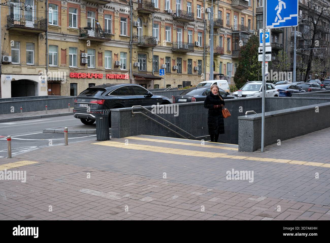 Eine Frau läuft die Treppe hinunter in eine belebte Straße voller Autos. 24. November 2025, Kiew, Ukraine, Schewtschenko Boulevard Stockfoto