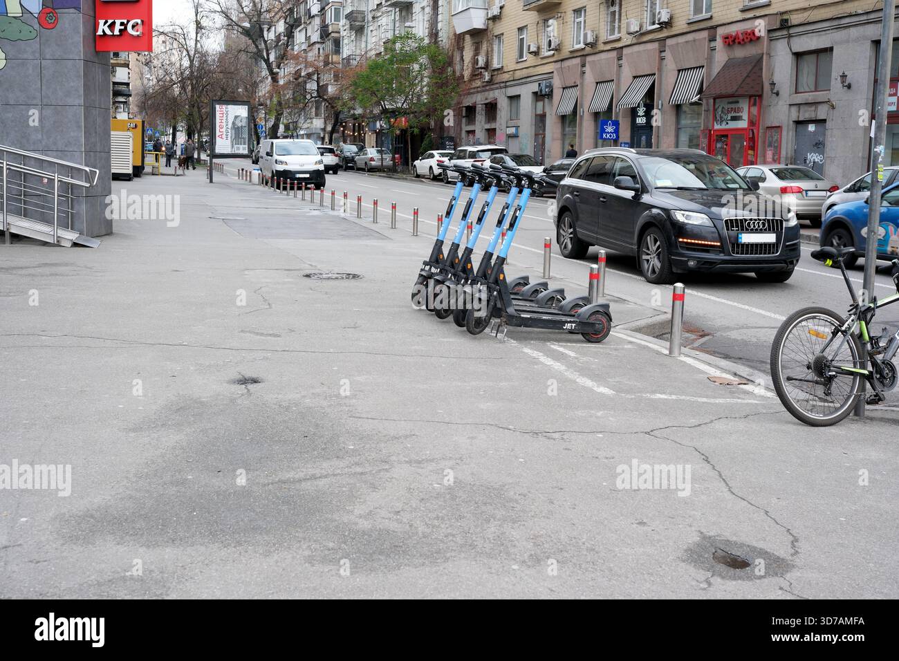 Eine Reihe von Elektrorollern wartet auf Fahrer auf einer stark befahrenen Stadtstraße in der Nähe von geparkten Autos. 24. November 2025 Kiew, Ukraine, Galitska-Platz. Stockfoto