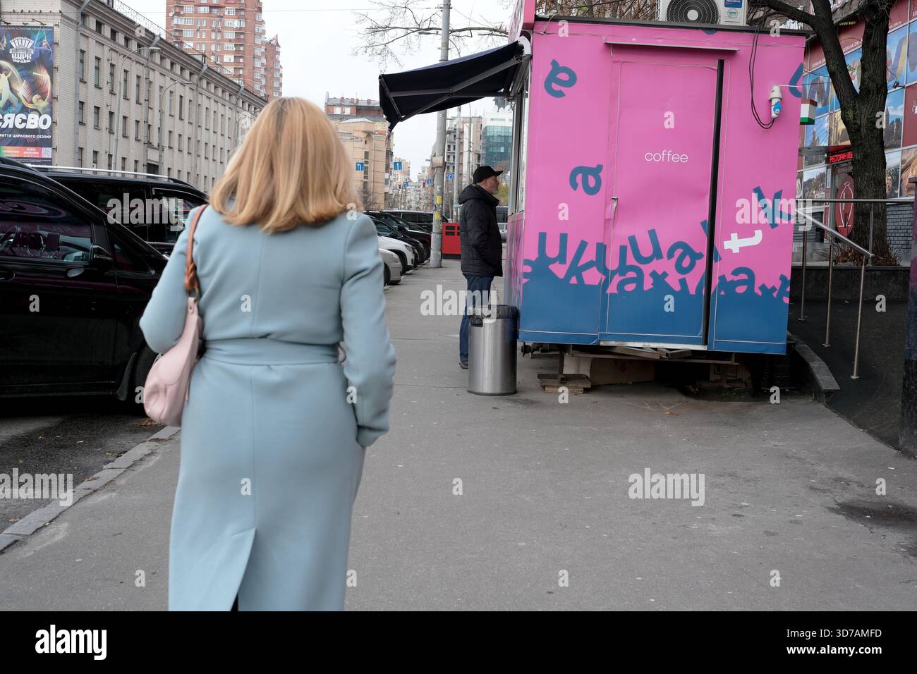 Eine Frau schlendert an einem lebhaften Kaffeewagen auf einer lebhaften Straße vorbei. 24. November 2025 Kiew, Ukraine, Galitska-Platz. Stockfoto