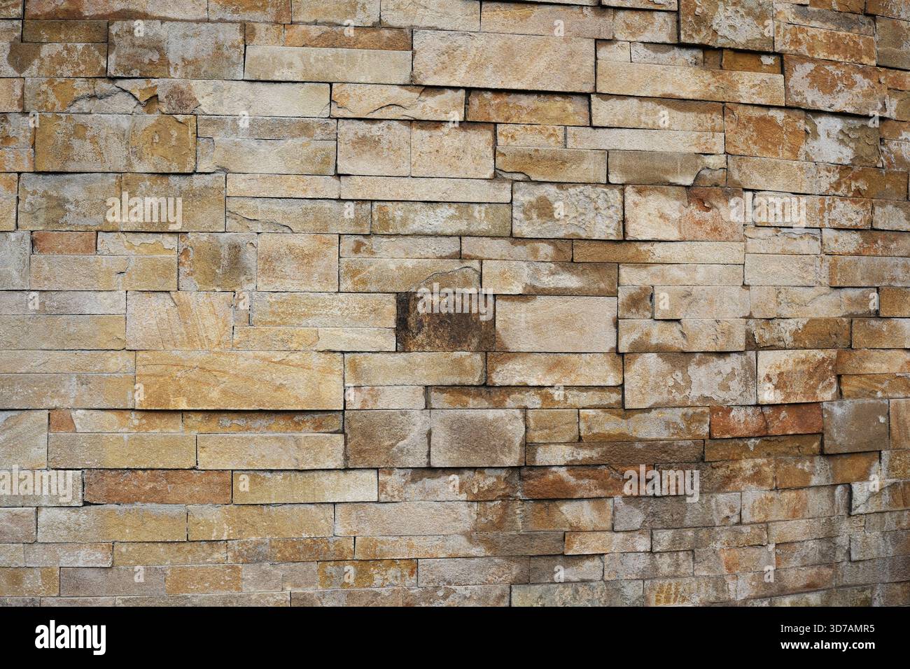 Quadratische Steine bilden eine warme, rustikale Mauer, die eine friedliche Atmosphäre im Freien fördert. Stockfoto