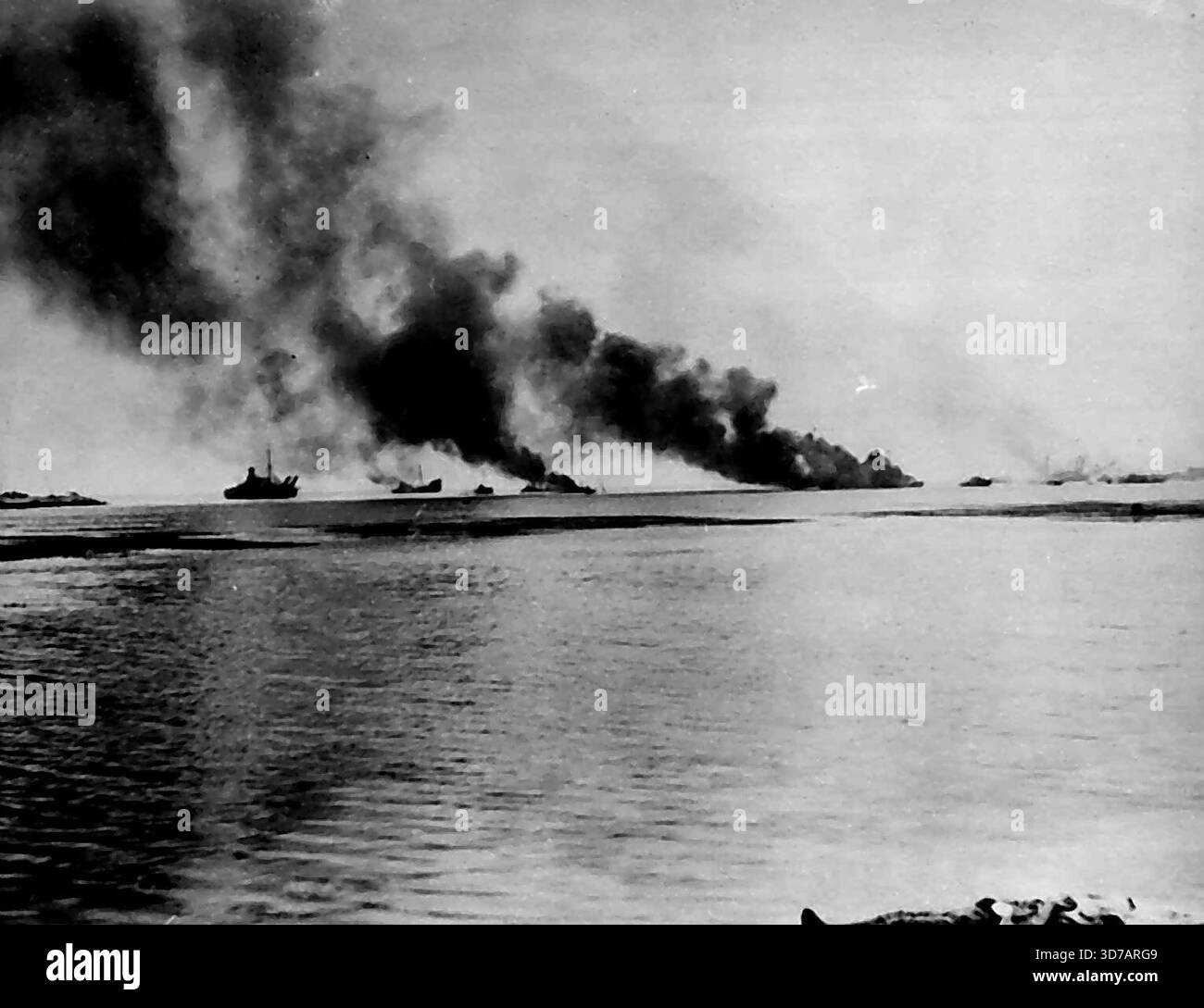 Jap-Fluchtversuch, der von Marines auf Saipan vereitelt wurde - japanische Schiffe schickten Rauchschwaden auf, nachdem sie von Marineartilleristen auf Saipan Island in den Marianen getroffen wurden, die einen Versuch vereitelten, die Jap-Truppen nördlich von Garapan zu evakuieren. Ein toter Jap-Krieger liegt am Ufer des Wassers, nachdem sein Versuch, die im Tanapag-Hafen verankerten Schiffe zu erreichen, ebenfalls geflügelt worden war. Juli 1944. (Foto von zugehörigem Pressefoto). Stockfoto