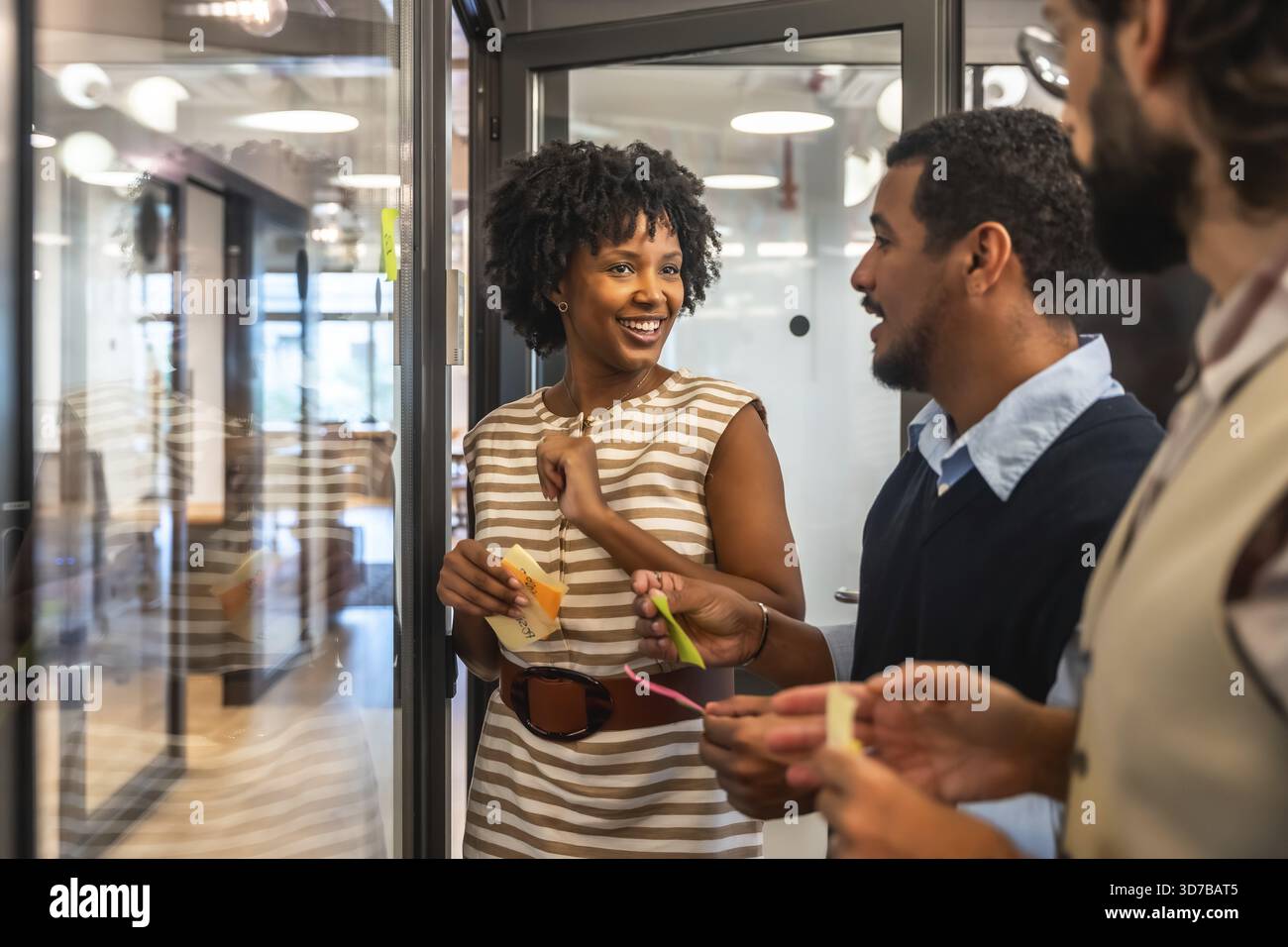 Verschiedene Geschäftsleute arbeiten während eines agilen Meetings zusammen, diskutieren kreative Konzepte und tauschen ihre Gedanken mit bunten Haftnotizen auf einem Glas aus Stockfoto