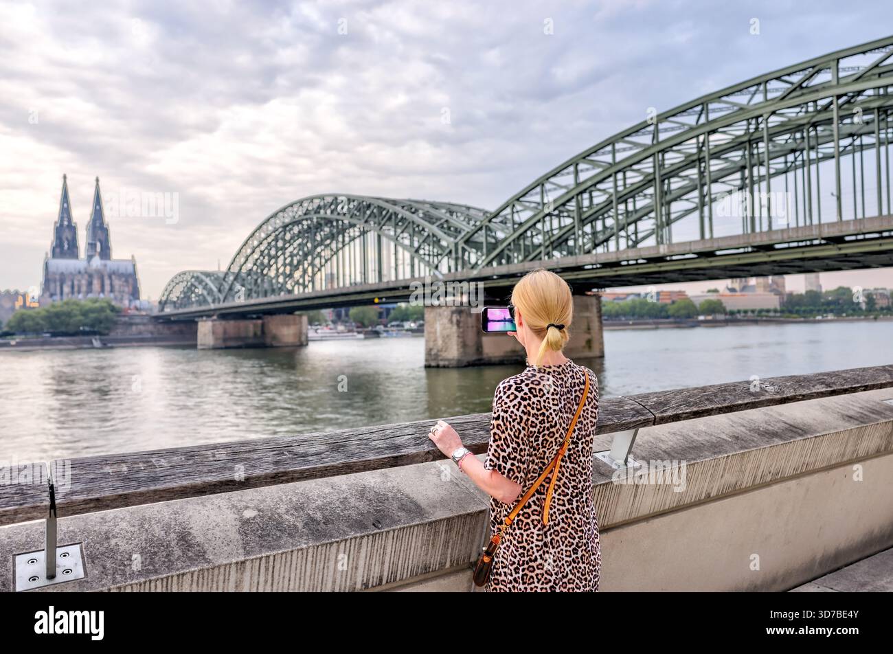 Eine Frau, die bei Sonnenaufgang die Hohenzollernbrücke und den Kölner Dom über den Rhein fotografiert Stockfoto