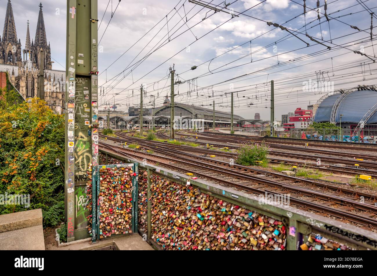 Bahngleise, die bei Sonnenaufgang bei bewölktem Himmel in Köln zur Hohenzollernbrücke und zum Dom führen Stockfoto
