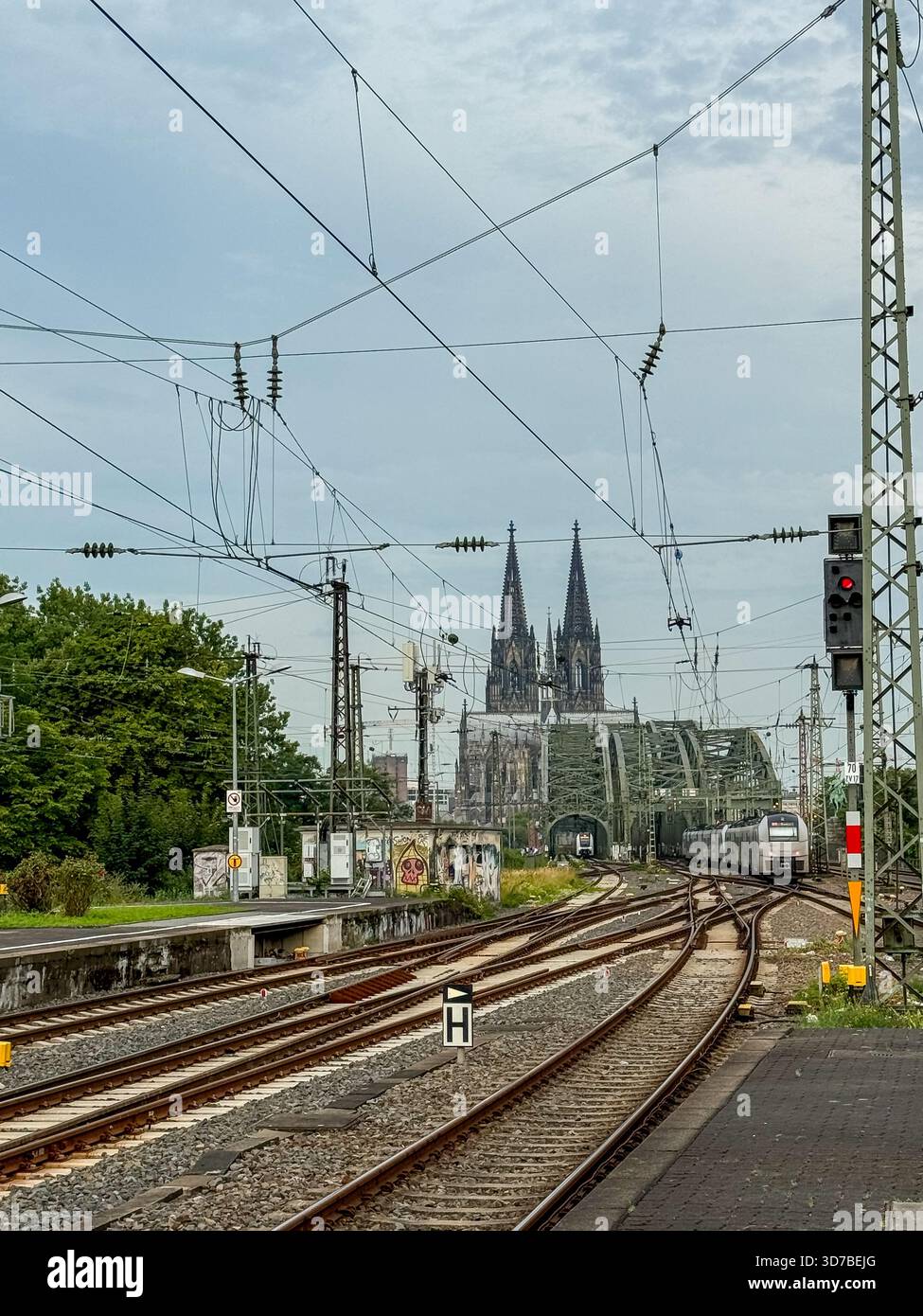 Bahngleise, die bei Sonnenaufgang bei bewölktem Himmel in Köln zur Hohenzollernbrücke und zum Dom führen Stockfoto