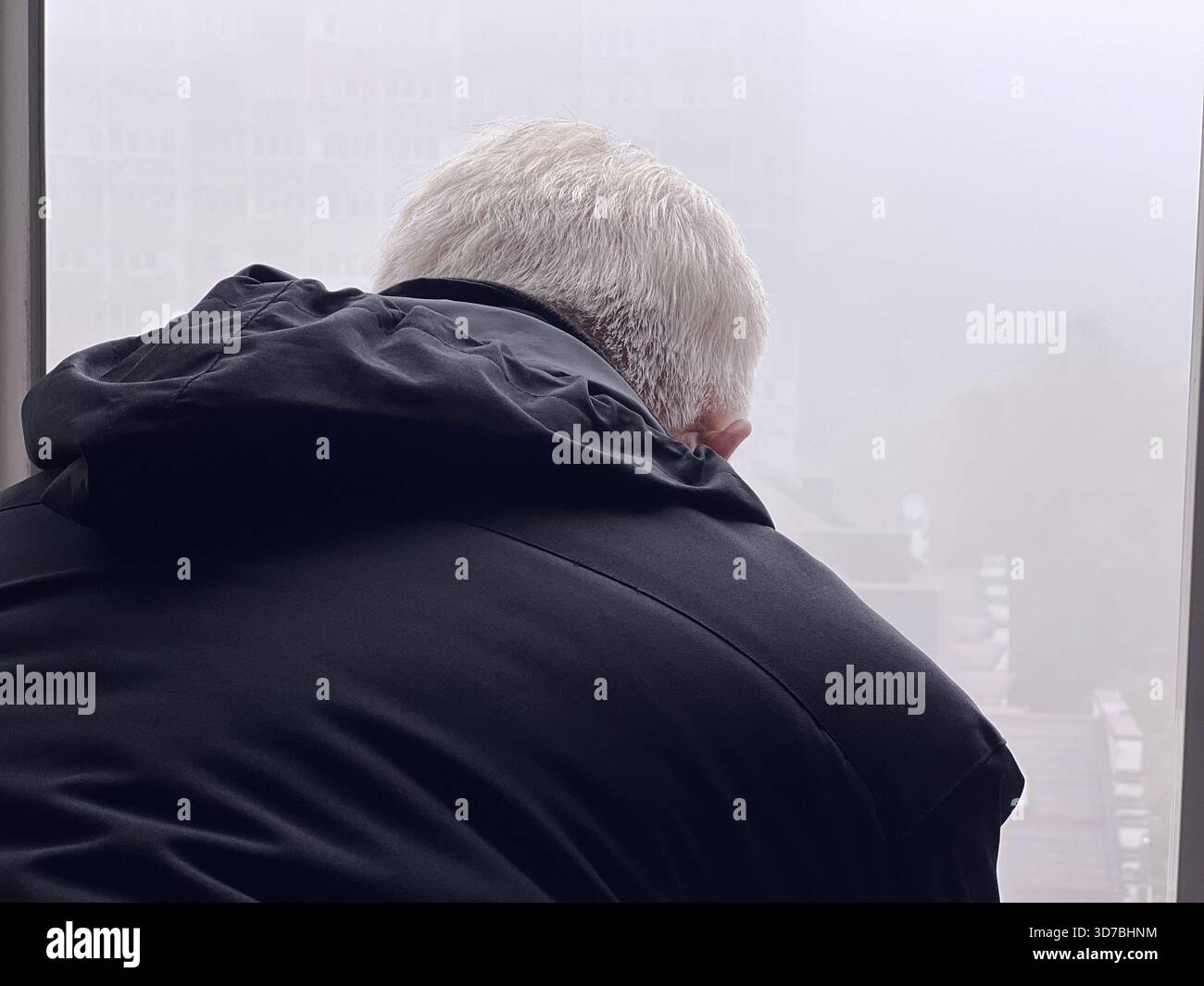 Ein grauhaariger Mann in einer Jacke schaut bei Nebel aus dem Fenster Stockfoto