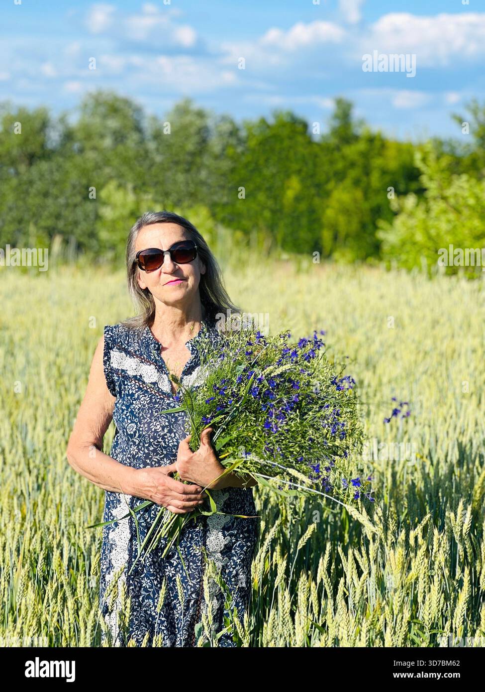 Attraktive Seniorin mit Blumenstrauß im Weizenfeld Stockfoto