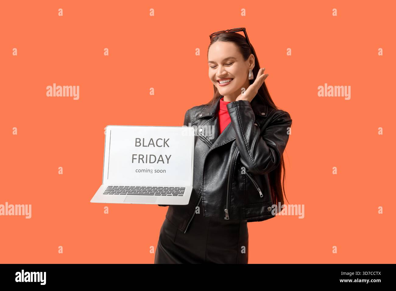 Glückliche junge Frau, die einen Laptop mit SCHWARZEM Text hält, DER BALD auf orangefarbenem Hintergrund ERSCHEINT Stockfoto
