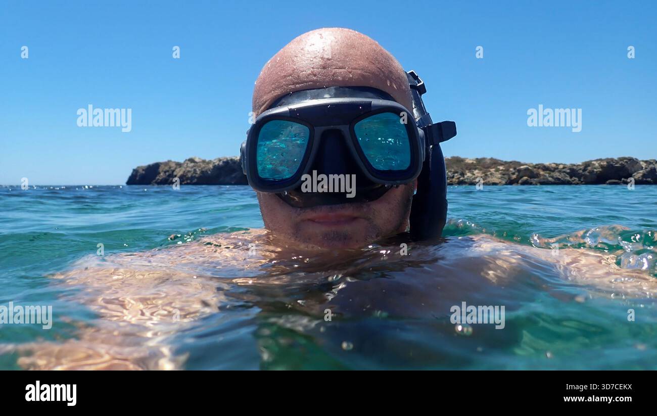 Mann mit Schnorchelmaske und Tuba mit dem Kopf knapp über dem wunderschönen blauen Meerwasser der Costa Blanca an einem sonnigen Tag. Stockfoto