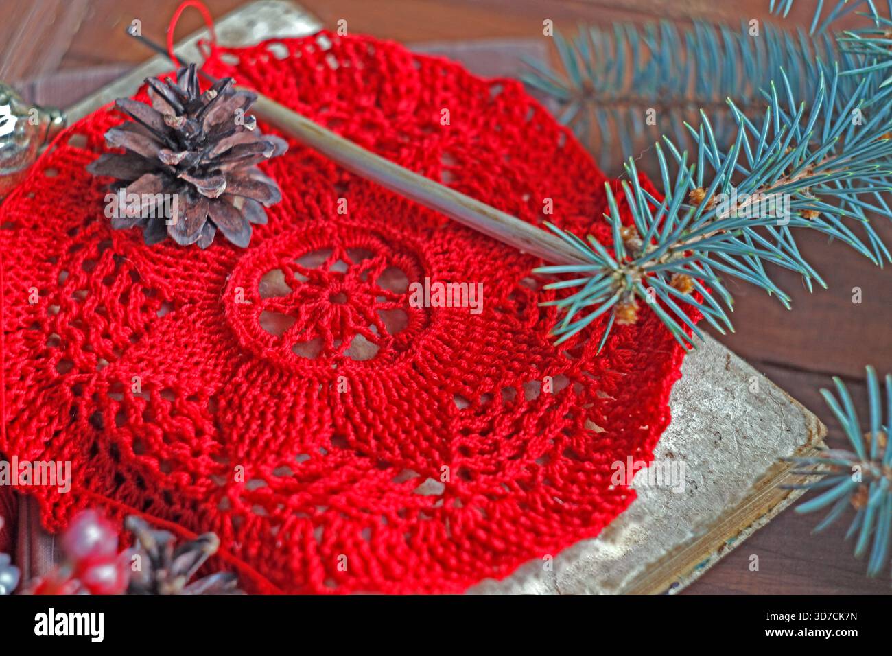 Rotes Weihnachtsdoly mit einem Tannenzapfen, Häkelnadel und Fichtenzweigen auf rustikalem Holzhintergrund häkeln. Handgefertigte Weihnachtsdekoration und festliches Kunsthandwerk Stockfoto