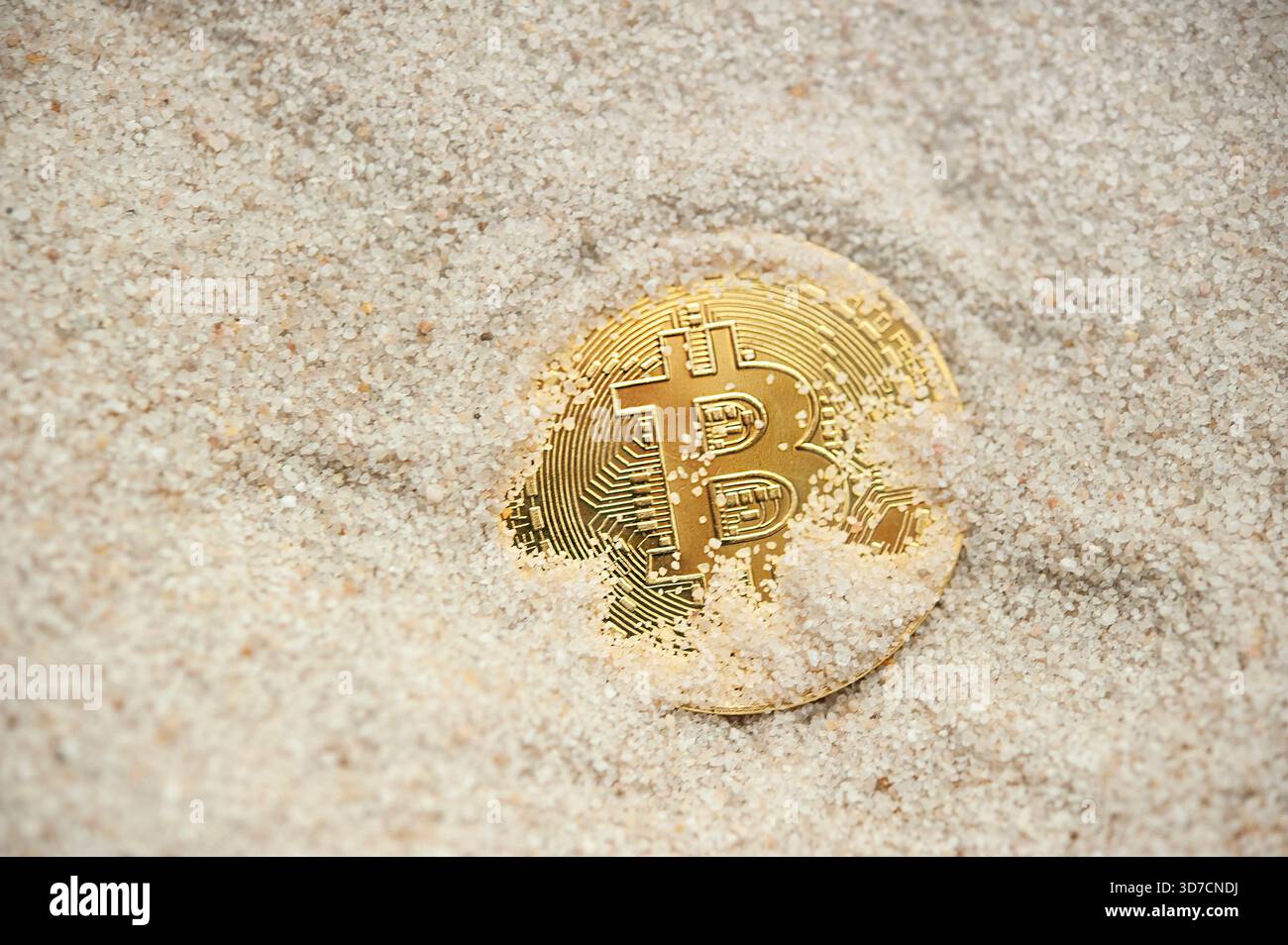 Goldbitcoin-Token, teilweise in Sand vergraben, symbolisiert verborgenen oder unsicheren Wert Stockfoto