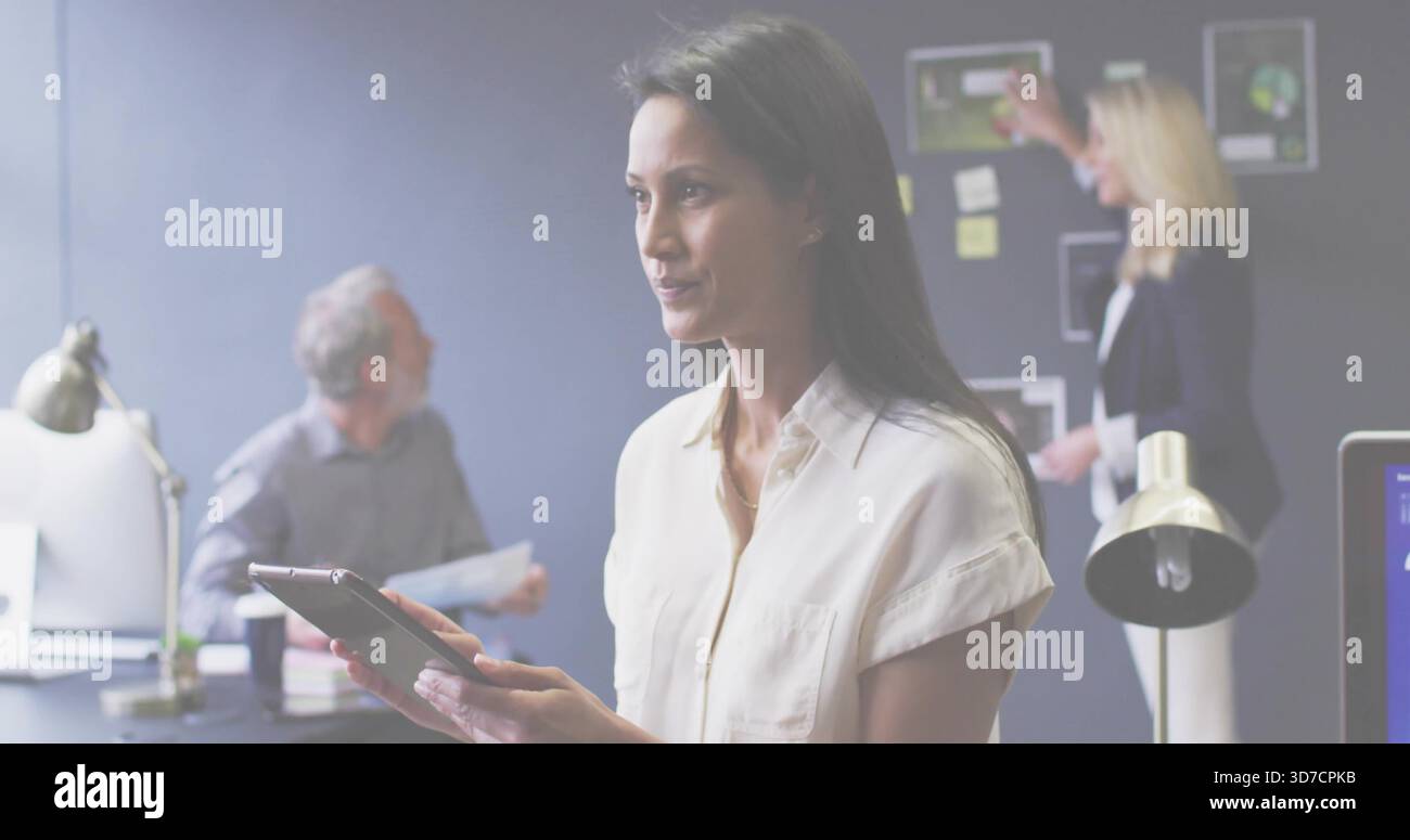 Mit Tablette, reife Frau in leichter Bluse, die die Planung im Büro vornimmt, mit angehefteten Diagrammen Stockfoto