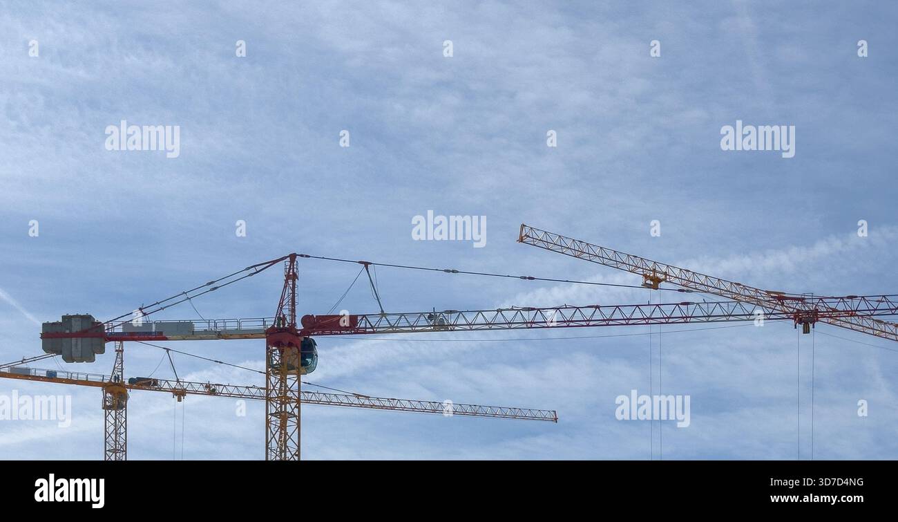Der Kran erhebt sich hoch gegen den blauen Himmel. Stahlbaumaschinen heben schwere Materialien auf städtebaulichem Gelände an und symbolisieren den industriellen Fortschritt in Mo Stockfoto