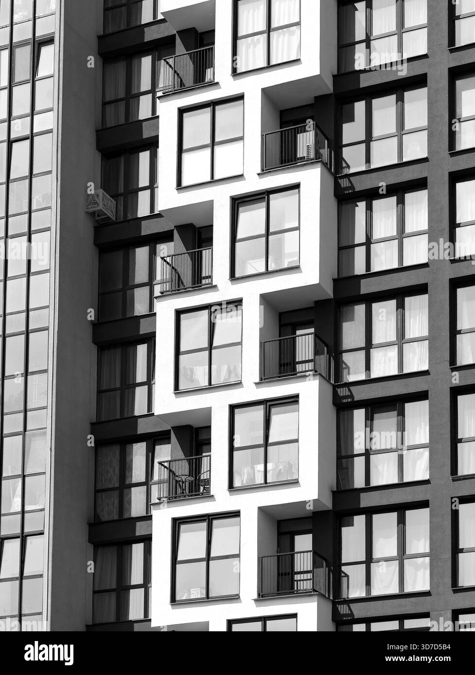Blick aus nächster Nähe auf die moderne Apartmentfassade mit geometrischem Balkondesign und großen Glasfenstern. Minimalistisches architektonisches Detail in zeitgenössischem Ambiente Stockfoto