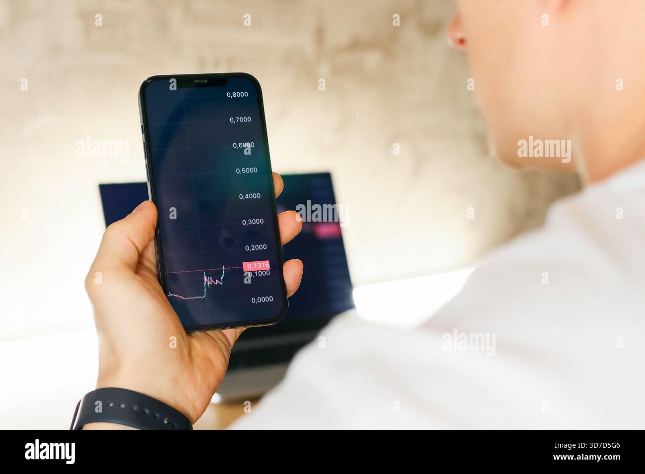 Die Hand einer Person, die ein Smartphone hält und ein horizontales Balkendiagramm mit sinkenden Werten anzeigt, der Laptop im Hintergrund ist weich fokussiert. Stockfoto