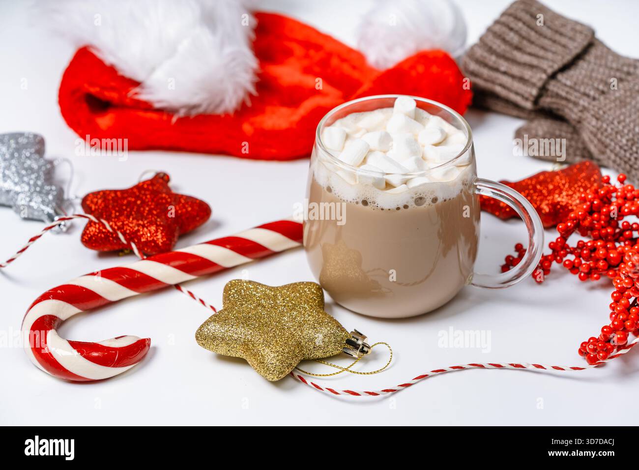Gemütliche Winterszene mit gestrickten Fäustlingen, roten Beeren, Weihnachtsschmuck, Zuckerrohr und einer Tasse Heißgetränk mit Marshmallows. Perfekt für einen Chri Stockfoto