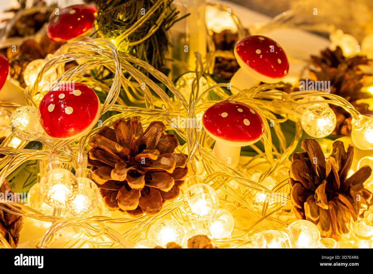 Weihnachtsdekoration und -Einrichtung. Eine glühende Girlande mit warmem Licht, Tannenzapfen und pilzförmigen Ornamenten. Stockfoto