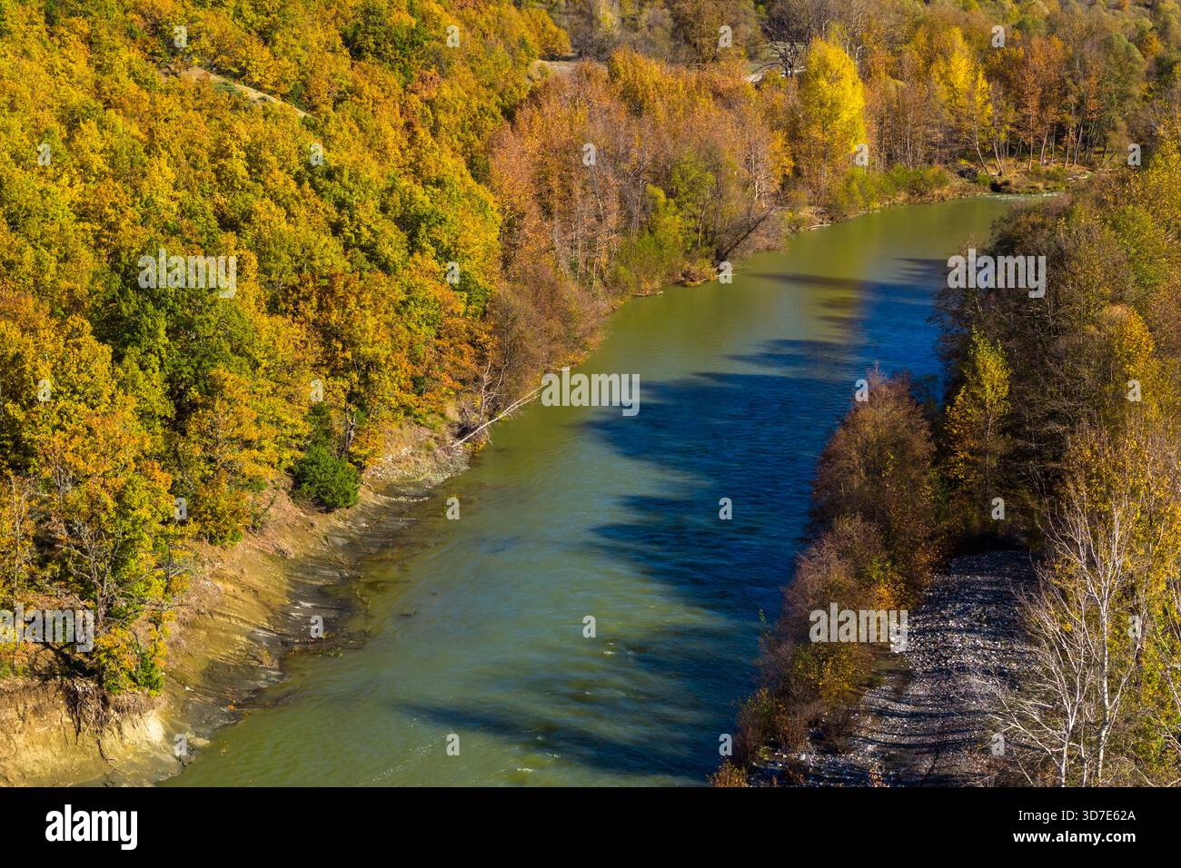 Aus der Vogelperspektive des Venezikos River, der sich durch den lebhaften Herbstwald in Westmakedonien, Griechenland, mit einer parallelen Straße, die in das natürliche Land mündet Stockfoto